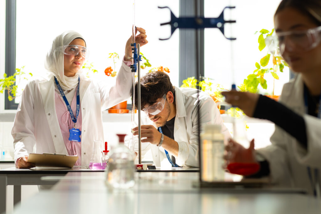 Three students work together in a bright, modern science classroom using laboratory equipment.